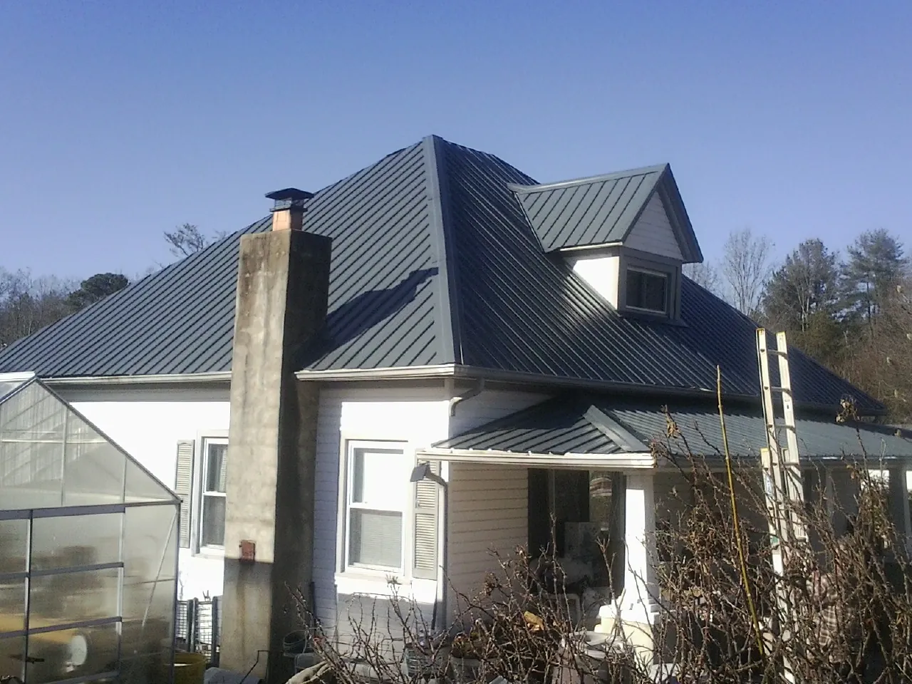 Dark blue standing seam metal roof on a white farmhouse with dormer — Slate & Tile Roof Repair by Roofing Brothers in Keene