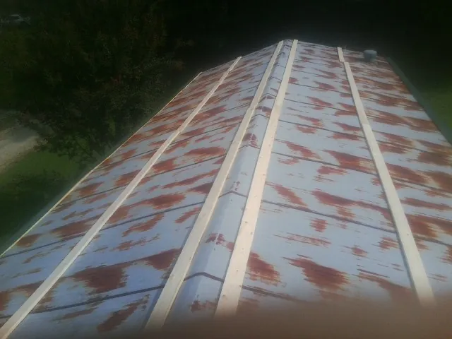 Rusted metal roof panels with new wood purlins before replacement in Keene