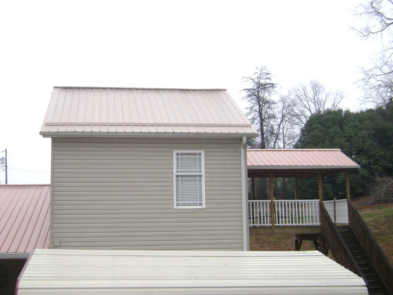 Tan metal roofs on a two story addition and attached porch, from a Roof Replacement job in Keene